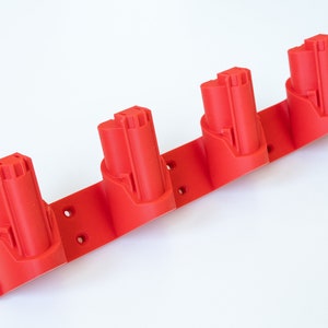 K&ouml;nnte beinhalten: Ein roter Batteriehalter zur Aufnahme von vier Elektrowerkzeugbatterien. Der Halter besteht aus Kunststoff und hat eine rechteckige Basis mit vier Batterief&auml;chern und Befestigungsl&ouml;chern. Die Batterien sind rot und zylindrisch.