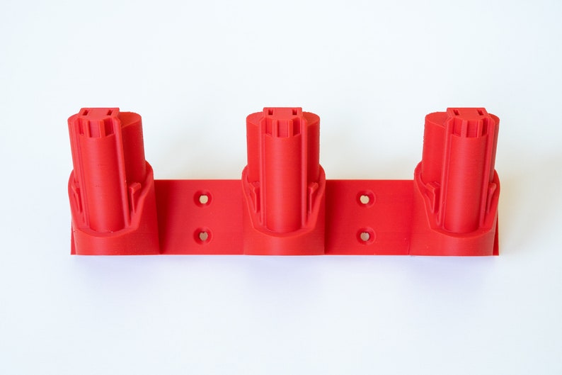 K&ouml;nnte beinhalten: Ein roter 3-fach Batteriehalter f&uuml;r Elektrowerkzeuge. Der Halter besteht aus Kunststoff und hat drei zylindrische Schlitze zur Aufnahme von Batterien. Der Halter ist f&uuml;r die Montage an einer Wand oder einer anderen Oberfl&auml;che konzipiert.