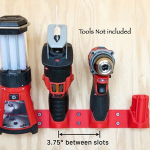 K&ouml;nnte beinhalten: Roter Werkzeughalter mit drei Schlitzen f&uuml;r Elektrowerkzeuge. Die Schlitze sind 9,5 cm voneinander entfernt. Der Text "Tools Not included" ist sichtbar. Der Halter ist auf einer hellen Holzoberfl&auml;che montiert.