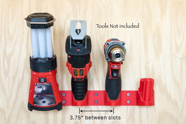 K&ouml;nnte beinhalten: Roter Werkzeughalter mit drei Schlitzen f&uuml;r Elektrowerkzeuge. Die Schlitze sind 9,5 cm voneinander entfernt. Der Text "Tools Not included" ist sichtbar. Der Halter ist auf einer hellen Holzoberfl&auml;che montiert.