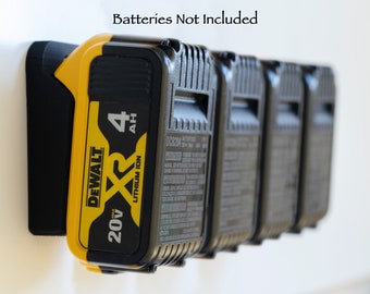 Puede incluir: Un soporte de batería negro montado en la pared con cinco baterías negras y amarillas de 20V XR Lithium Ion. Las baterías están etiquetadas con "4 AH". El texto "Batteries Not Included" está encima del soporte.