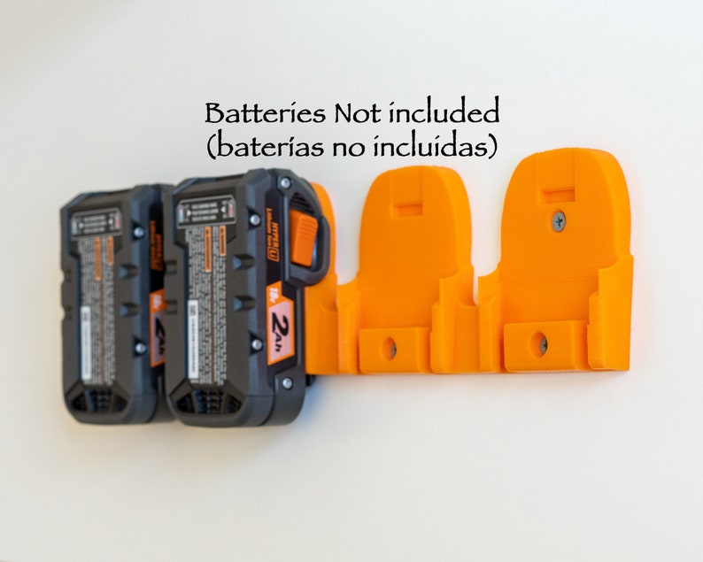 Puede incluir: Un soporte de bater&iacute;a naranja impreso en 3D montado en una pared blanca, que sostiene tres bater&iacute;as de herramientas el&eacute;ctricas negras y grises. El texto "Batteries Not included" es visible.