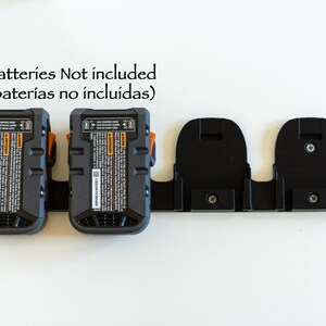 Puede incluir: Un paquete de bater&iacute;as negro y naranja con un soporte negro. El paquete de bater&iacute;as tiene una etiqueta con texto y est&aacute; conectado a un soporte negro con dos ranuras. El texto "Batteries Not included" est&aacute; encima del paquete de bater&iacute;as.
