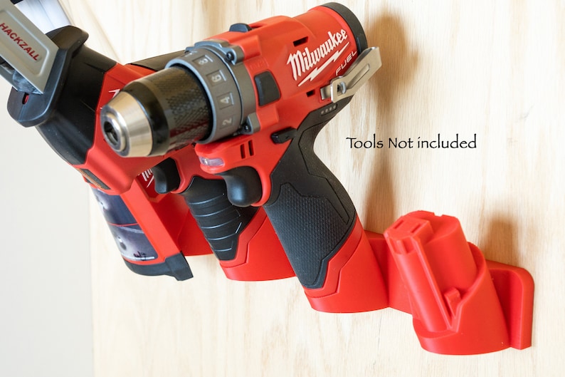K&ouml;nnte beinhalten: Rote und schwarze Werkzeugaufbewahrung an einer hellen Holzoberfl&auml;che. Der Halter h&auml;lt eine Bohrmaschine und eine S&auml;bels&auml;ge. Der Text "Tools Not included" ist sichtbar.