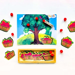 May include: A colorful educational game for kids featuring a tree with red apples, baskets with numbers, and red pom-poms. The game is designed to help children learn to count and match numbers.