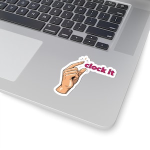 May include: A sticker featuring a hand pinching with the text "clock it" in a pink font. The hand is depicted with a light skin tone and is outlined in black. The sticker is placed on a silver laptop.