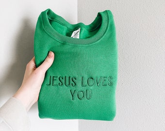 May include: A green sweatshirt with the text "JESUS LOVES YOU" embroidered in black.