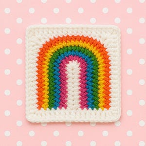 Może przedstawiać: Kwadratowy, kremowy element wykonany na szydełku z kolorowym wzorem tęczy. Tęcza rozciąga się przez środek, prezentując pasma czerwieni, pomarańczy, żółci, zieleni, błękitu i różu. Tło jest jasnoróżowe z białymi kropkami.