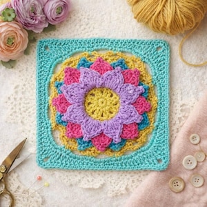 May include: A square, colorful crochet piece with a floral design. The center is yellow, surrounded by purple, pink, and blue petals, all framed by a turquoise border. Yarn, scissors, and buttons are in the background.