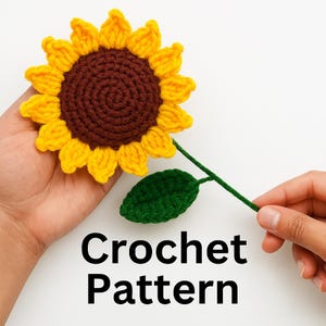 Op de afbeelding: Een gehaakte zonnebloem met gele bloemblaadjes, een bruin centrum en een groene stengel en blad. De tekst "Crochet Pattern" wordt eronder weergegeven.