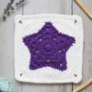 May include: A square, white crochet piece with a large, purple star in the center. The star has a detailed, openwork design. The piece is likely a decorative item or part of a larger craft project.