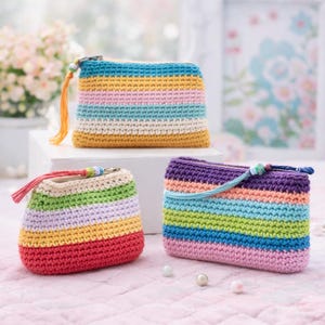 May include: Three colorful, crocheted zipper pouches in a variety of sizes. Each pouch features horizontal stripes in shades of blue, yellow, pink, green, and purple. The pouches have a tassel or cord attached to the zipper.