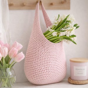 K&ouml;nnte beinhalten: Eine hellrosa geh&auml;kelte Tragetasche mit wei&szlig;en Blumen. Links steht eine Vase mit rosa Tulpen. Eine Kerze mit Holzdeckel und dem Text "Peony Blush" steht rechts auf einem gewebten Untersetzer.
