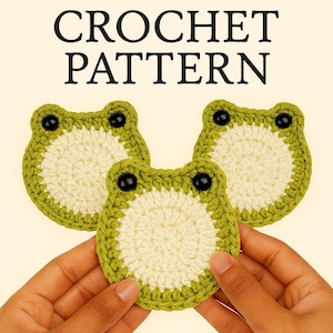 May include: Three handmade crochet frog-shaped coasters. Each coaster features a cream-colored center, a green border, and black button eyes. The text "CROCHET PATTERN" is displayed at the top of the image.