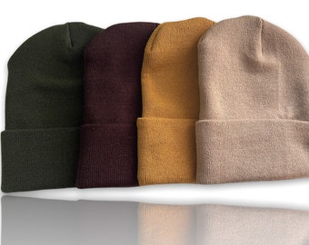 May include: Four knit beanies in different colors: olive green, burgundy, mustard yellow, and beige.