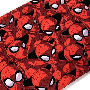 May include: Red fabric with a repeating pattern of Spiderman's face. The fabric has a black background and the Spiderman faces are red with black webbing and white eyes.
