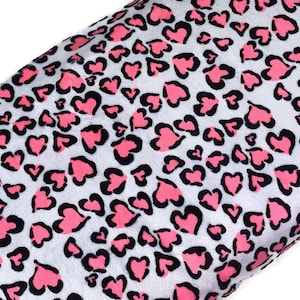 May include: A soft fabric featuring a repeating pattern of pink hearts outlined in black, set against a white background. The design mimics an animal print style with the heart shapes arranged in a dense, scattered layout across the material surface.