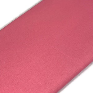 May include: A close-up shot of a folded piece of fabric in a solid, muted rose color. The fabric has a subtle texture and appears to be a medium-weight material. The edges are clean and crisp, with a white background.