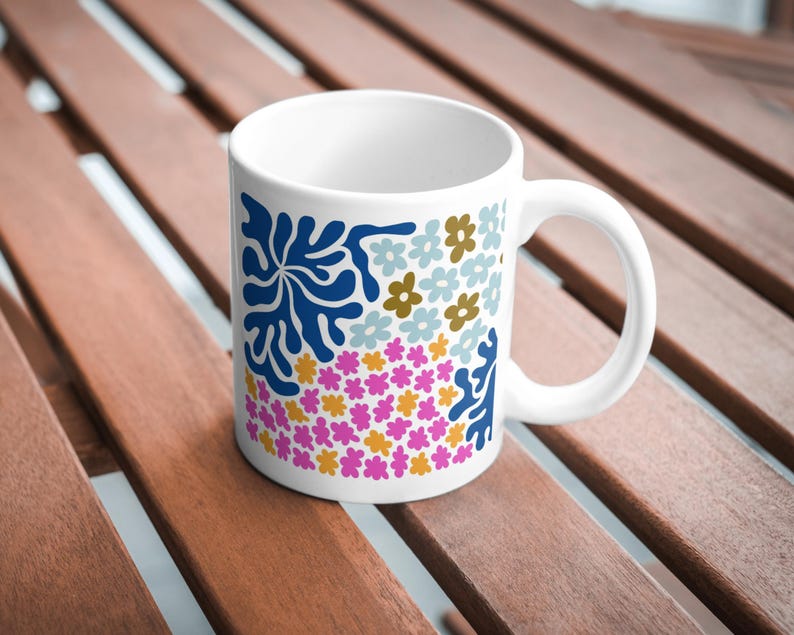 Puede incluir: Taza de cer&aacute;mica blanca con un dise&ntilde;o floral y abstracto colorido. El dise&ntilde;o presenta flores azules, rosas, amarillas y blancas, as&iacute; como una forma abstracta azul.