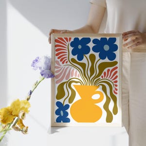 Puede incluir: Una impresi&oacute;n floral abstracta colorida con flores azules en un jarr&oacute;n amarillo. La impresi&oacute;n est&aacute; enmarcada en un marco de madera claro.