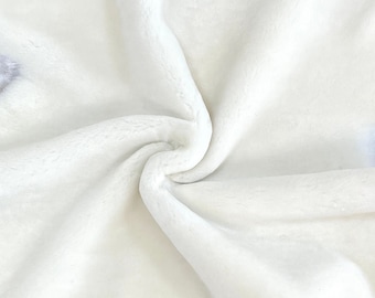 Puede incluir: Una alfombra de piel de oveja blanca con una textura suave y esponjosa. La alfombra está doblada en espiral y tiene un borde natural irregular.