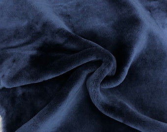 Puede incluir: Una piel de oveja azul oscuro con una textura suave y peluda. La piel está doblada y drapeada sobre una superficie de madera.