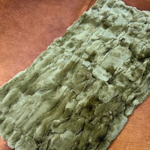 May include: A soft, plush green faux fur throw blanket with a textured, wavy pattern. The blanket is laid out on a brown and white cowhide rug.