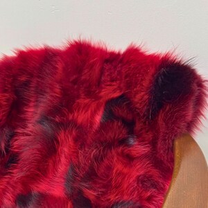 May include: A red faux fur throw rug with black accents. The rug is draped over a wooden chair.