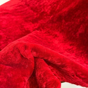 Peut inclure: Gros plan sur un tissu rouge duveteux avec une texture douce et moelleuse. Le tissu est pli&eacute; et drap&eacute;, montrant la texture et la couleur.