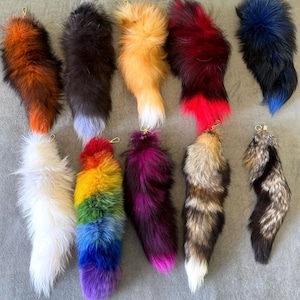 Può includere: Dieci code di pelliccia sintetica colorate con portachiavi. Le code sono di vari colori, tra cui arancione, nero, marrone, rosso, blu, bianco, arcobaleno, viola e grigio.