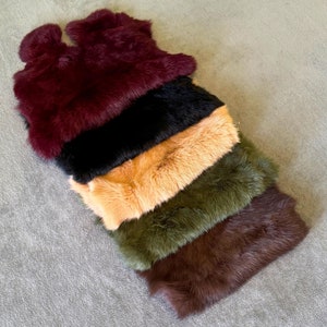 Op de afbeelding: Vijf bont sjaals in verschillende kleuren, op elkaar gestapeld. De sjaals zijn bordeauxrood, zwart, oranje, groen en bruin.