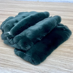 May include: A stack of three dark green faux fur fabric strips. The fabric is soft and plush.