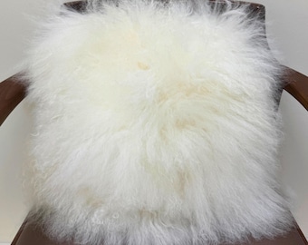 Puede incluir: Un cojín de piel de oveja blanca y esponjosa sobre una silla de cuero marrón.