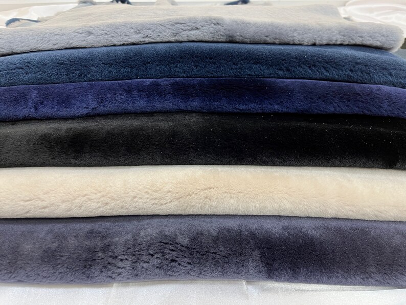 May include: A stack of six faux fur fabric swatches in various shades of blue, black, and white. The fabric is soft and plush.