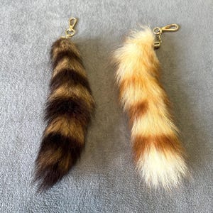 May include: Two faux fur keychains with a striped pattern. One keychain is brown and black, the other is light brown and tan.