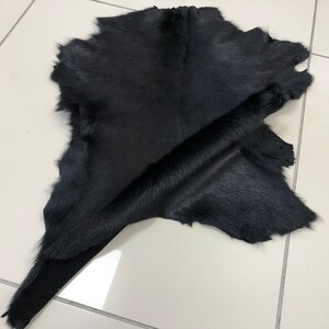 May include: A black cowhide rug with a soft, smooth texture. The hide is folded in half, revealing the underside.
