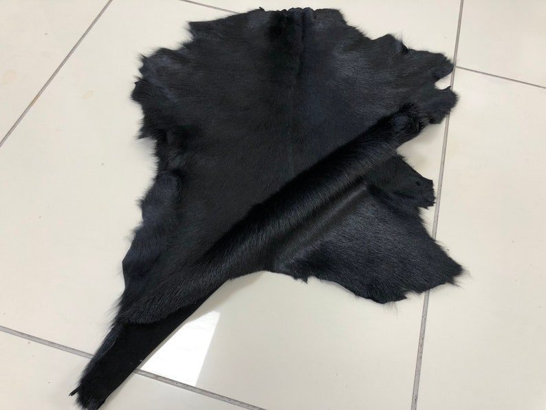 May include: A black cowhide rug with a soft, smooth texture. The hide is folded in half, revealing the underside.