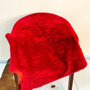 Peut inclure: Un tapis en peau de mouton rouge vif drap&eacute; sur une chaise en bois. Le tapis est doux et moelleux, avec une surface l&eacute;g&egrave;rement textur&eacute;e.