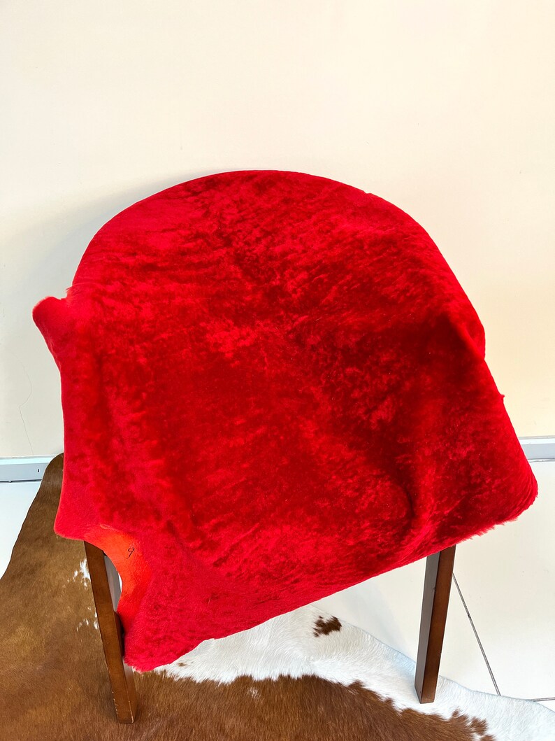 Peut inclure: Un tapis en peau de mouton rouge vif drap&eacute; sur une chaise en bois. Le tapis est doux et moelleux, avec une surface l&eacute;g&egrave;rement textur&eacute;e.