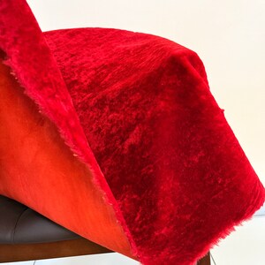 Peut inclure: Gros plan sur un tissu de velours rouge avec un bord effiloch&eacute;. Le tissu est drap&eacute; sur une chaise brune.