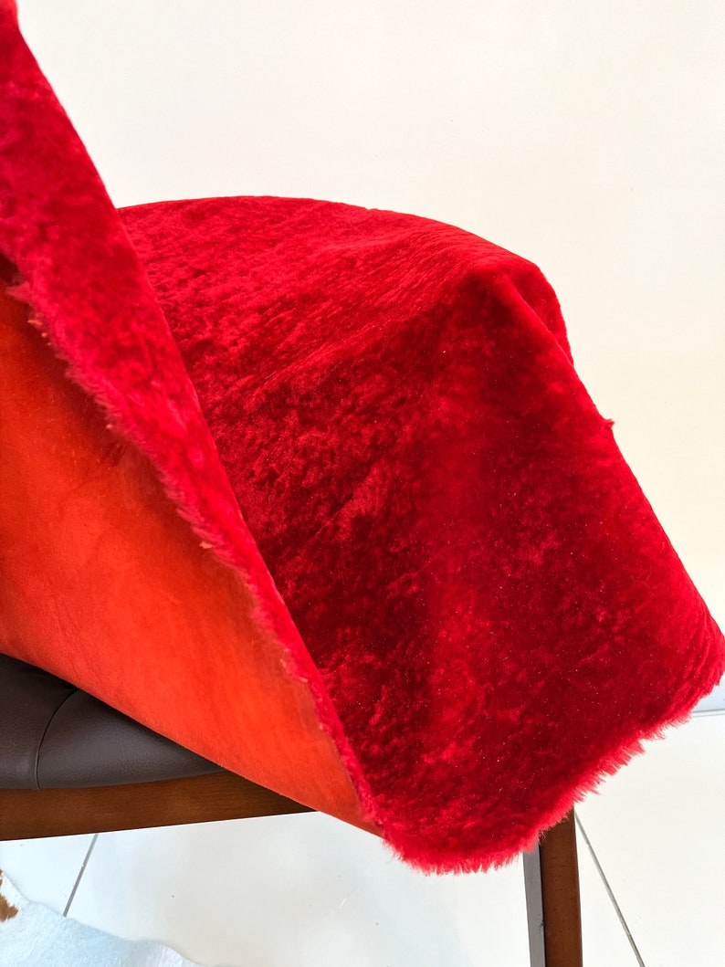 Peut inclure: Gros plan sur un tissu de velours rouge avec un bord effiloch&eacute;. Le tissu est drap&eacute; sur une chaise brune.