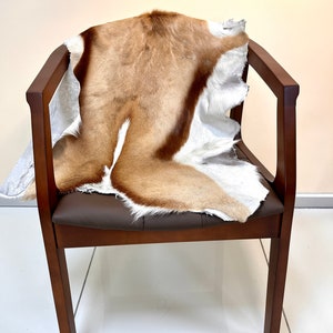 Op de afbeelding: Een bruine houten stoel met een bruine leren zitting en een bruin en wit dierenvachtkleed erop.