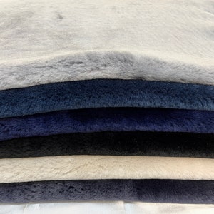 May include: A stack of six faux fur fabric swatches in various shades of blue, gray, and white. The fabric has a soft, plush texture.