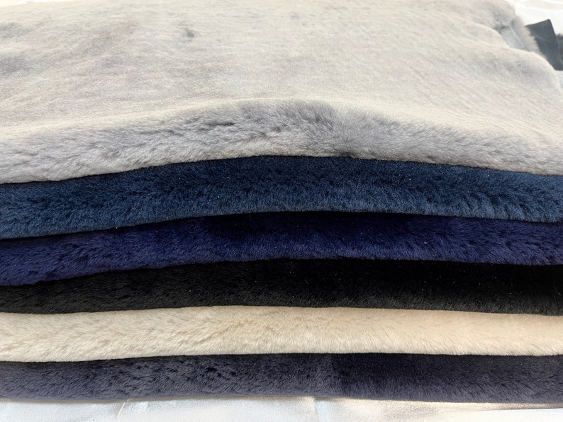 May include: A stack of six faux fur fabric swatches in various shades of blue, gray, and white. The fabric has a soft, plush texture.