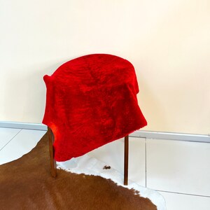 Peut inclure: Un tissu de velours rouge drap&eacute; sur une chaise en bois avec un tapis en peau de vache brun et blanc sur le sol.