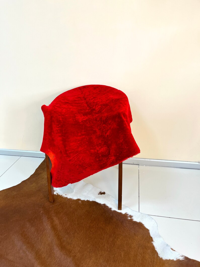 Peut inclure: Un tissu de velours rouge drap&eacute; sur une chaise en bois avec un tapis en peau de vache brun et blanc sur le sol.