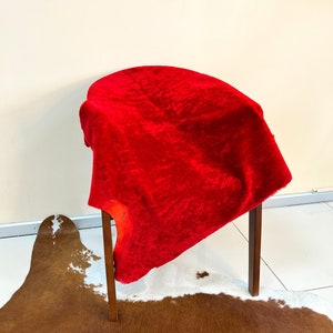 Peut inclure: Un tissu de velours rouge drap&eacute; sur une chaise en bois avec un tapis en peau de vache brun et blanc en dessous.