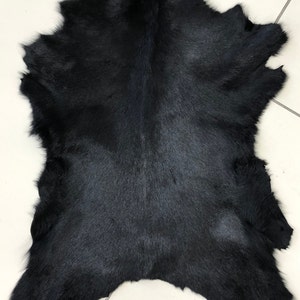 May include: A black cowhide rug with a natural, soft texture. The hide is laid flat on a white tiled surface.