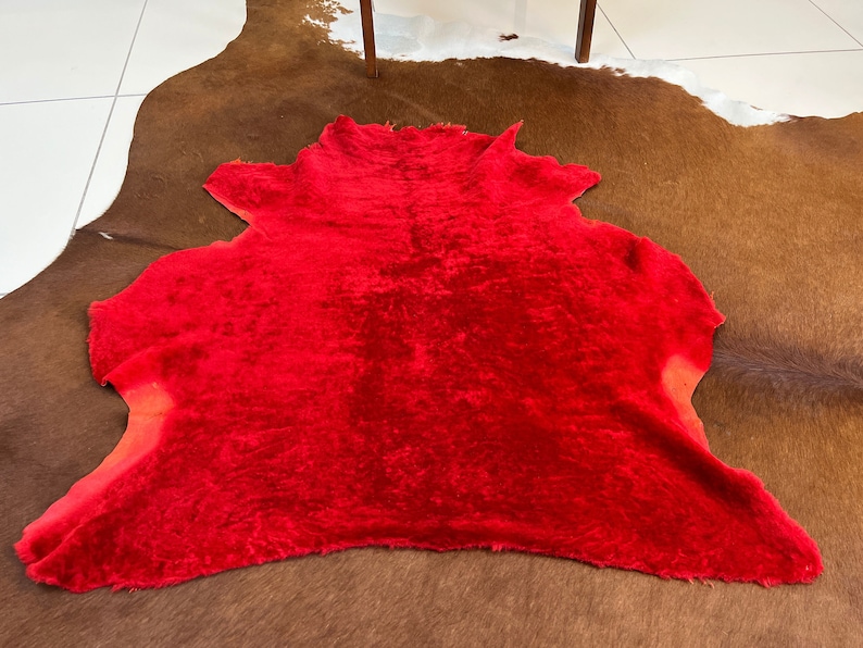 Peut inclure: Un tapis moelleux rouge vif avec une texture douce et velout&eacute;e. Le tapis est pos&eacute; sur un tapis en peau de vache brune et blanche.