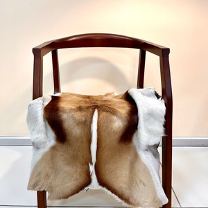 Op de afbeelding: Een bruine houten stoel met een wit en bruin dierenvachtkleed over de zitting gelegd.